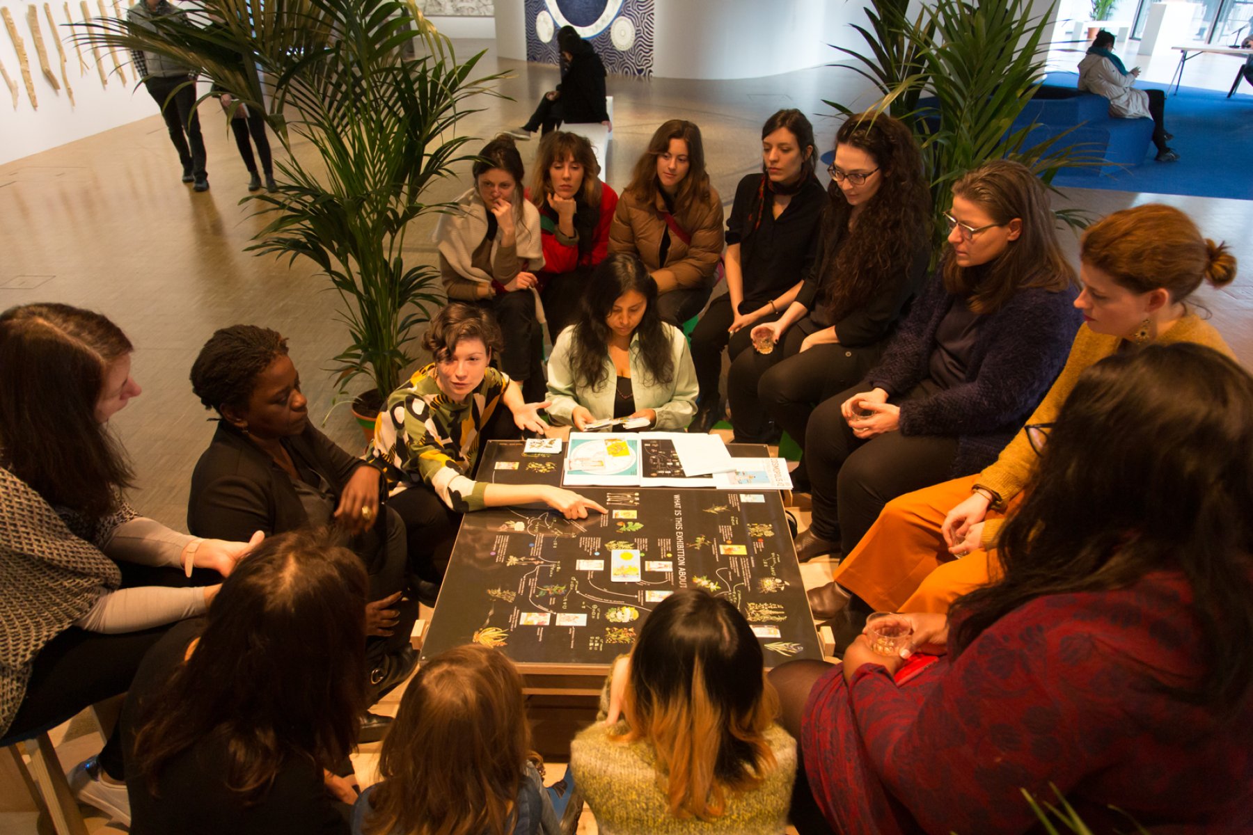 Women and children in Cosmosopolis art space sitting in thought around a poster laid flat on a table.jpg