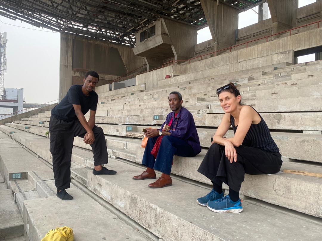Kathryn Weir, Folakunle Oshun and man sitting in empty concrete stadium.JPG